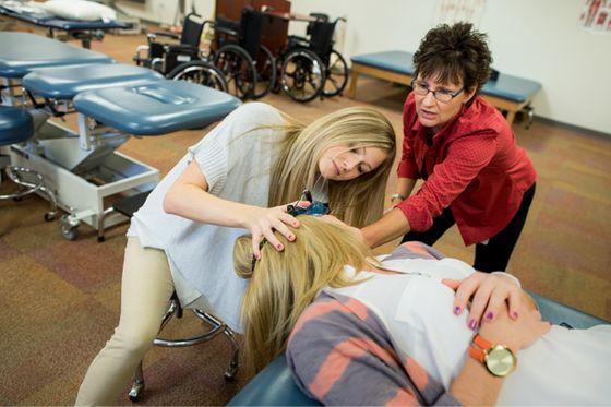 An instructor aids a student performing physical therapy on a patient